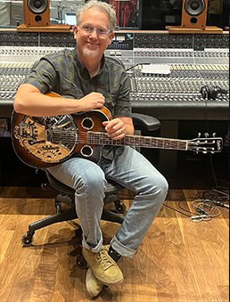 Bryan Sutton sitting in a studio holding a Dobrato resophonic guitar.